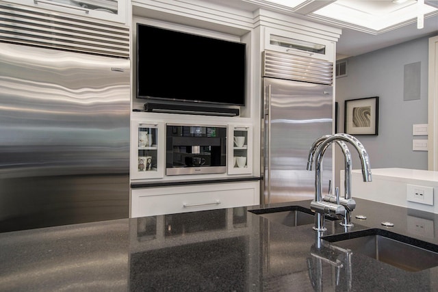 kitchen with built in refrigerator, dark stone countertops, visible vents, and white cabinets