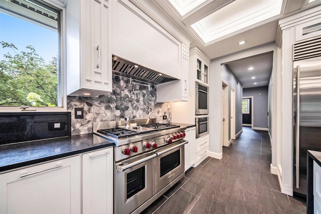 kitchen featuring high end appliances, dark countertops, tasteful backsplash, white cabinets, and premium range hood