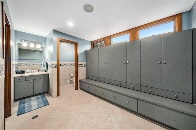 bathroom with vanity, visible vents, tile walls, and wainscoting