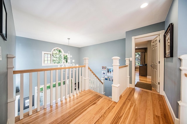 hallway featuring baseboards, wood finished floors, an upstairs landing, a chandelier, and recessed lighting