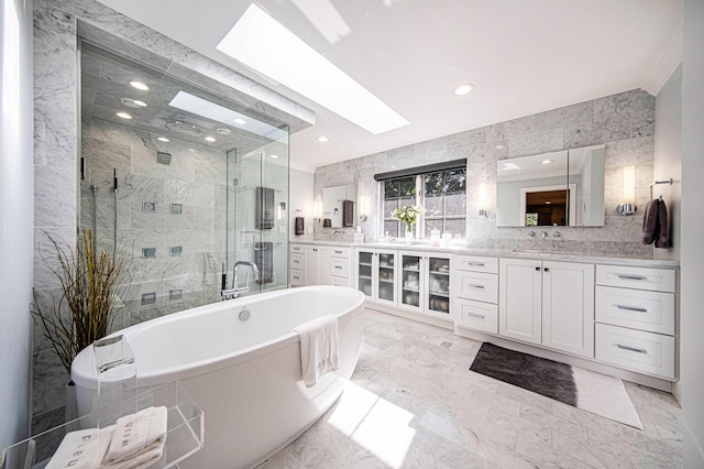 full bath with a skylight, marble finish floor, a freestanding bath, a stall shower, and vanity