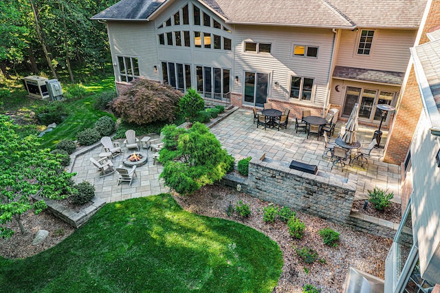 rear view of property featuring brick siding, roof with shingles, a fire pit, and a patio