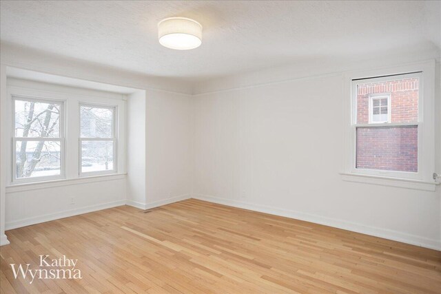 spare room featuring light wood-type flooring, a textured ceiling, and baseboards