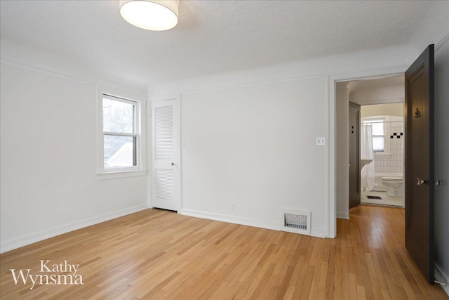 empty room with light wood-type flooring, visible vents, a textured ceiling, and baseboards