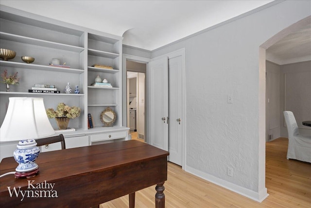 office featuring arched walkways, a textured wall, light wood finished floors, and baseboards