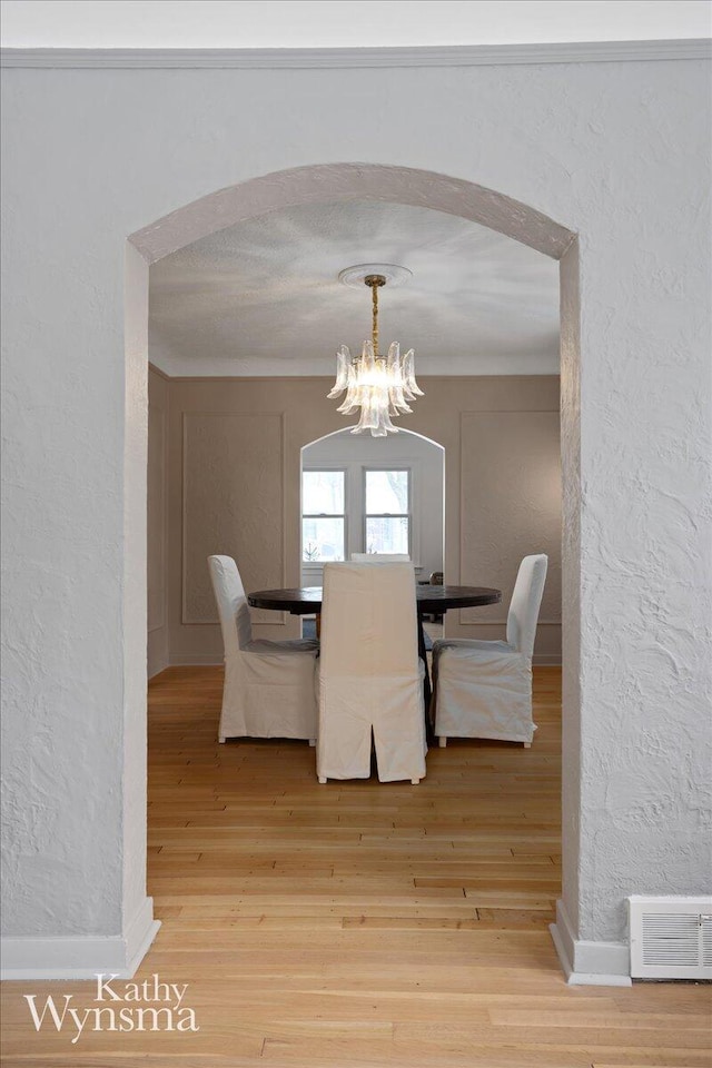 dining room with a chandelier, arched walkways, a textured wall, and light wood finished floors