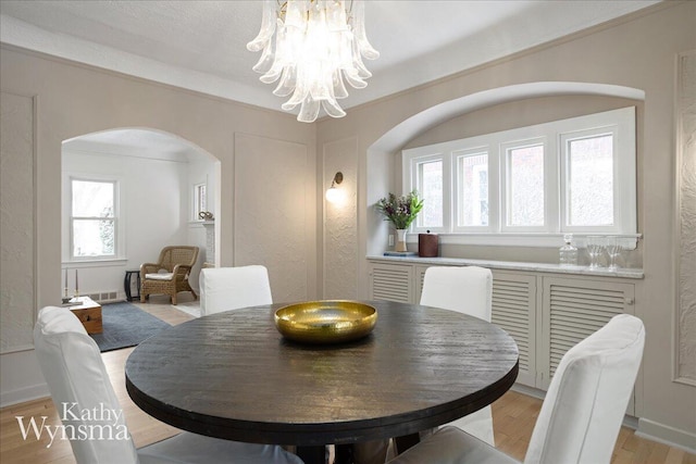 dining room featuring arched walkways, crown molding, light wood finished floors, visible vents, and an inviting chandelier