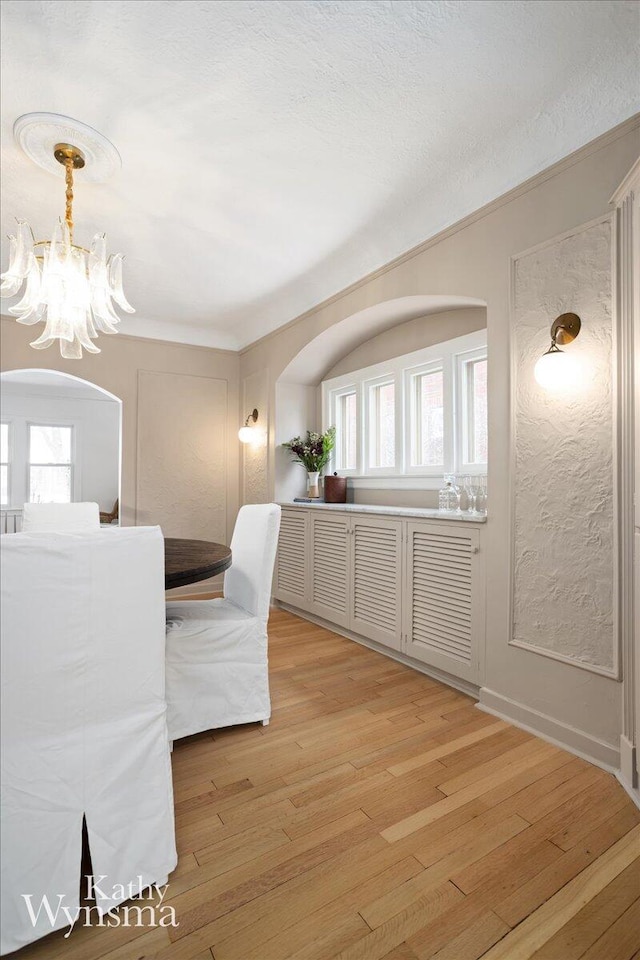 dining area with arched walkways, ornamental molding, a textured ceiling, light wood-type flooring, and a chandelier