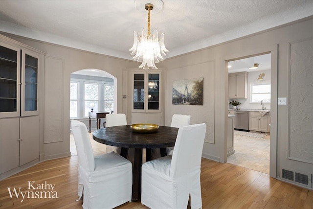 dining area with an inviting chandelier, light wood-style flooring, visible vents, and arched walkways