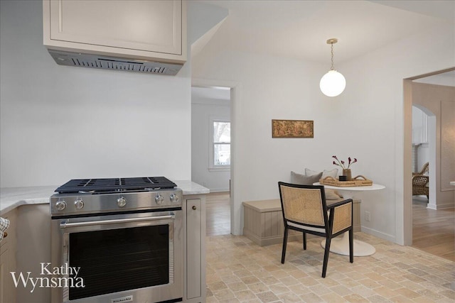 kitchen featuring arched walkways, brick floor, baseboards, hanging light fixtures, and stainless steel range with gas cooktop