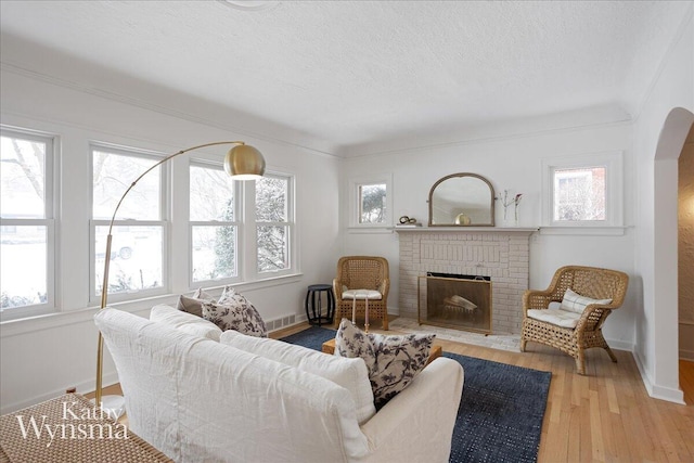 living room featuring baseboards, visible vents, wood finished floors, a textured ceiling, and a fireplace