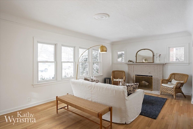 living area with a textured ceiling, a brick fireplace, hardwood / wood-style flooring, and baseboards