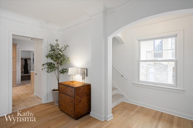 hall featuring light wood-style floors, baseboards, stairs, and arched walkways