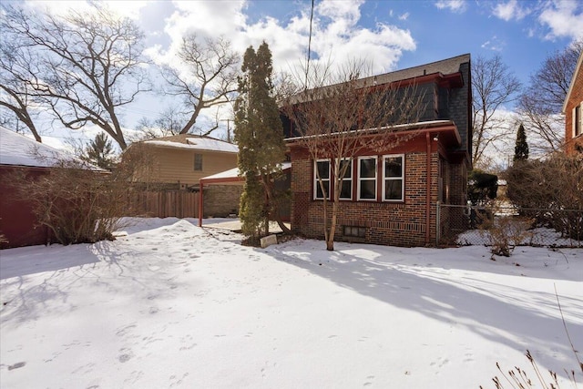 snow covered rear of property with brick siding and fence