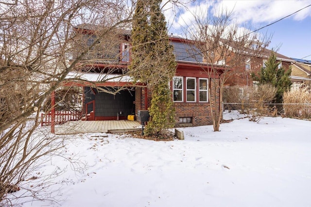 snow covered rear of property featuring brick siding and fence