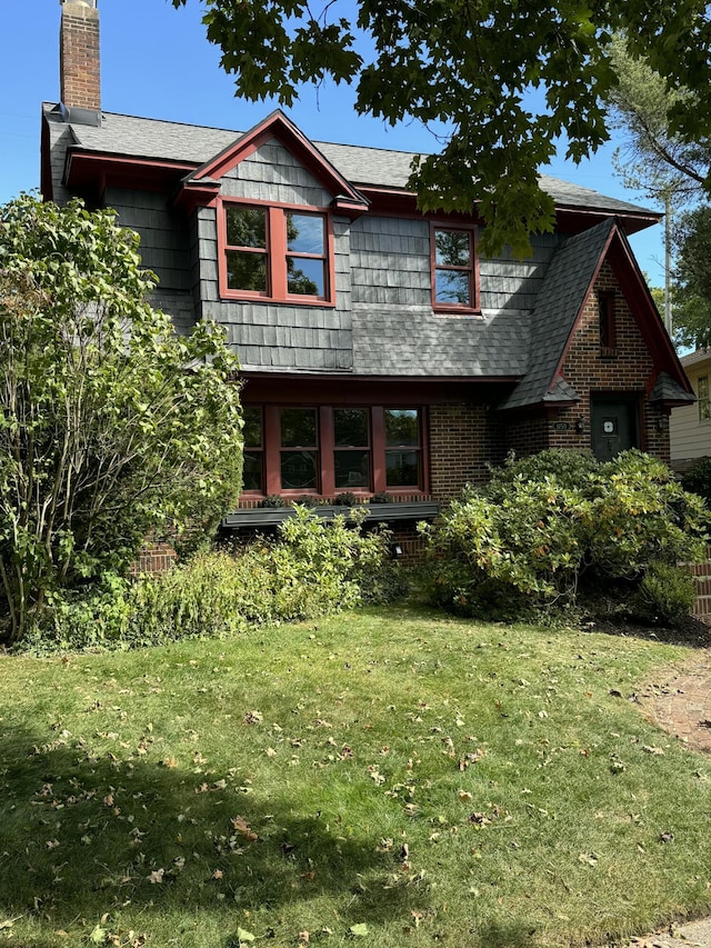 view of front facade with a chimney, a front lawn, and brick siding