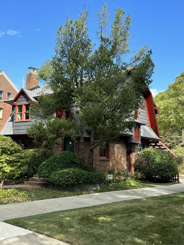 view of front facade with brick siding, a chimney, and a front yard