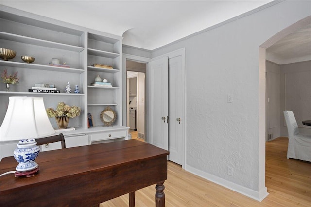 home office featuring arched walkways, a textured wall, light wood finished floors, and baseboards