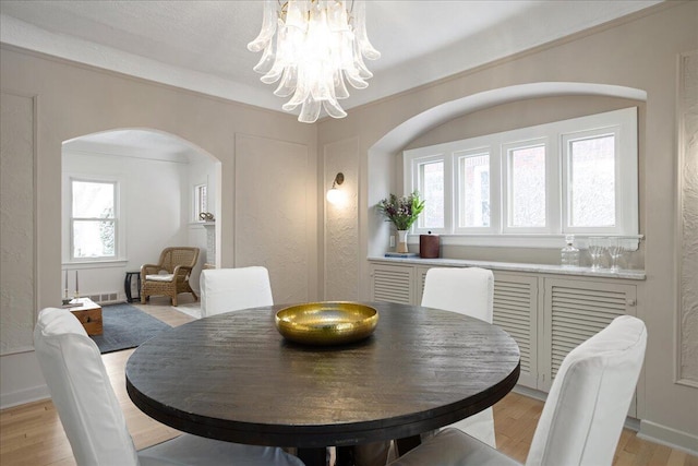 dining room with arched walkways, light wood finished floors, crown molding, and an inviting chandelier