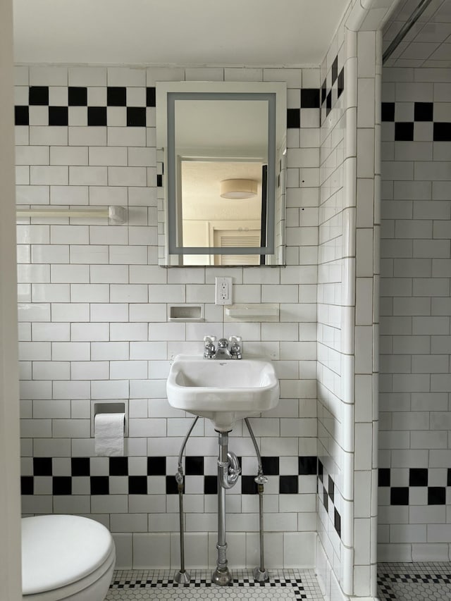 bathroom with toilet, a sink, backsplash, and tile walls