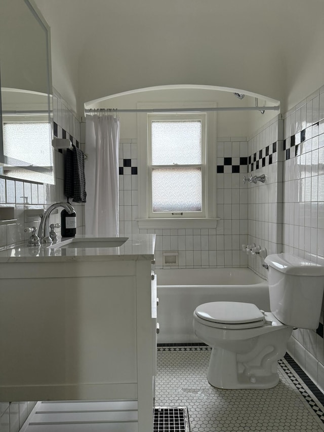 full bathroom featuring toilet, tile patterned flooring, shower / bath combination with curtain, vanity, and tile walls