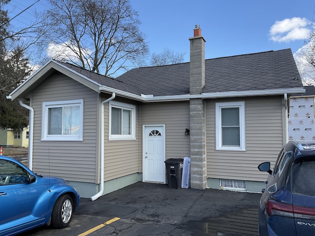 view of front of house with uncovered parking, a shingled roof, and a chimney