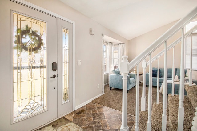 foyer with lofted ceiling, stone finish flooring, stairs, and baseboards