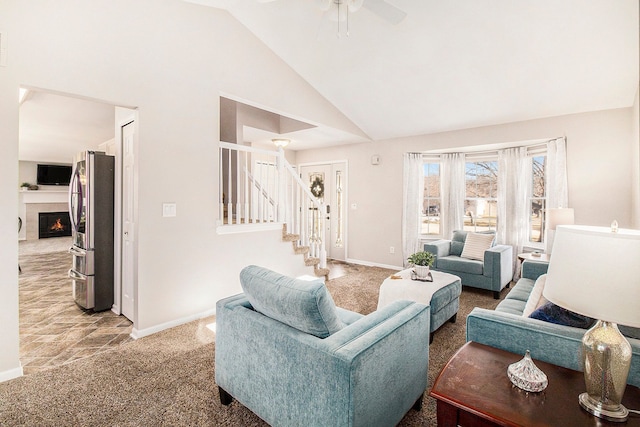 living room with baseboards, light colored carpet, stairway, a lit fireplace, and high vaulted ceiling