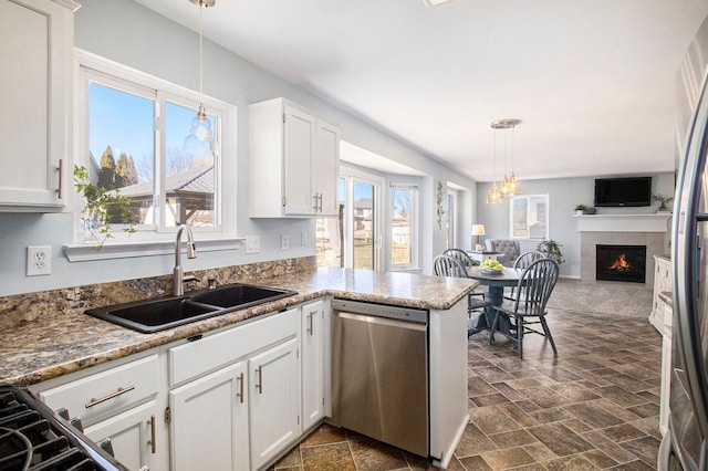 kitchen with stainless steel appliances, a sink, white cabinetry, open floor plan, and a tiled fireplace