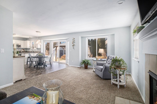 carpeted living area with baseboards, plenty of natural light, a sink, and a tiled fireplace