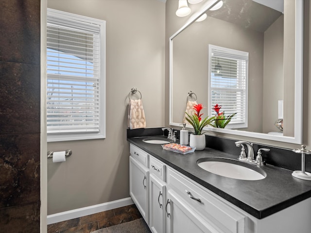 full bathroom featuring double vanity, stone finish flooring, baseboards, and a sink