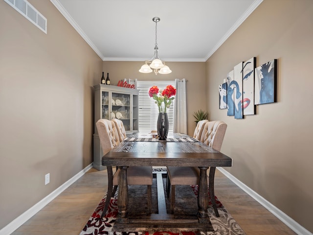 dining room featuring crown molding, a notable chandelier, visible vents, wood finished floors, and baseboards