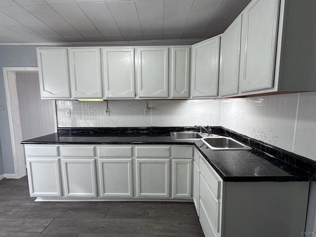 kitchen with decorative backsplash, dark countertops, dark wood-style flooring, white cabinetry, and a sink