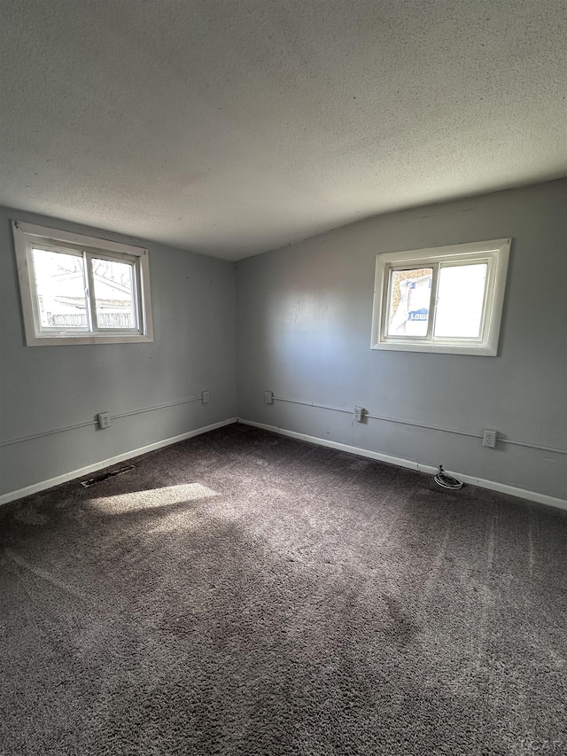 spare room with plenty of natural light, dark carpet, and a textured ceiling