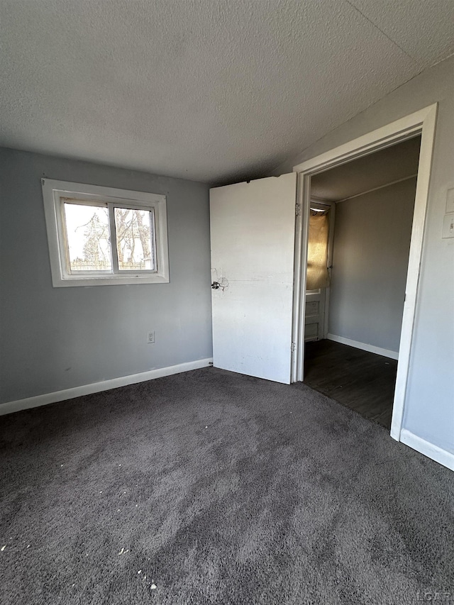 unfurnished bedroom featuring baseboards, dark colored carpet, and a textured ceiling