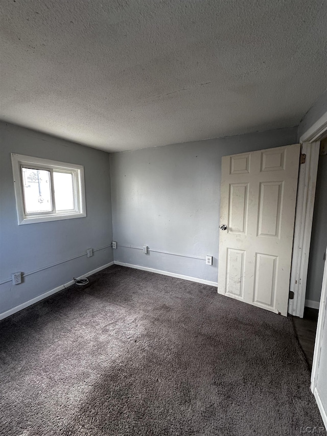 spare room with a textured ceiling, dark carpet, and baseboards