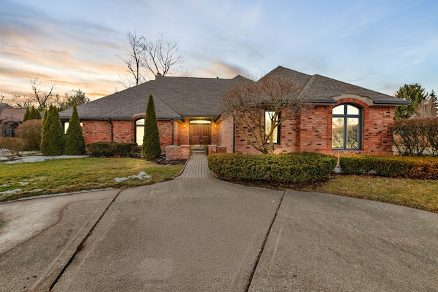 french country inspired facade with brick siding, roof with shingles, and a front yard