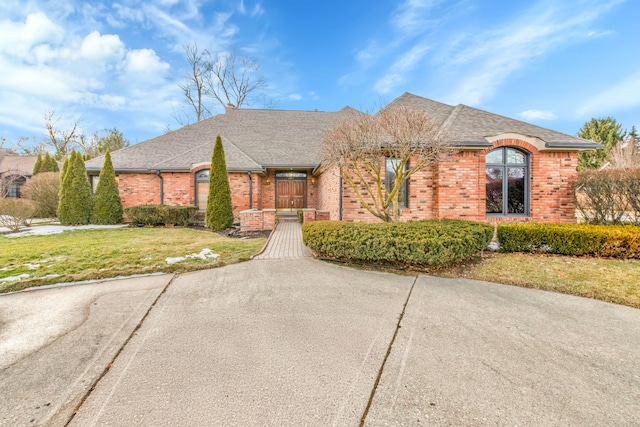 french country home with a shingled roof, a front yard, and brick siding