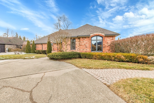 view of front of house featuring a front yard, brick siding, and roof with shingles