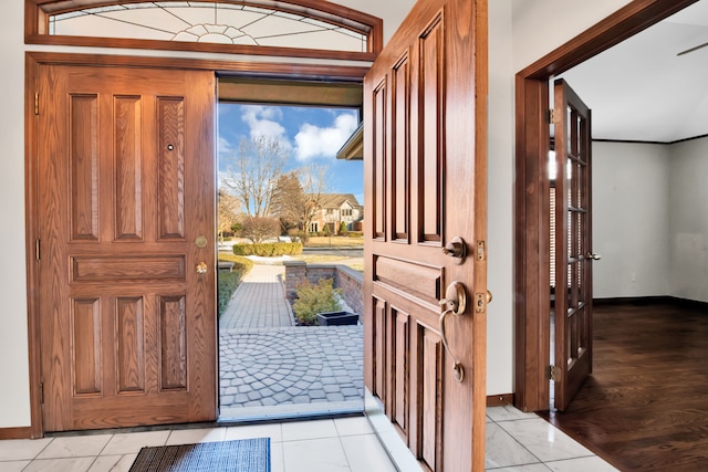 foyer with light tile patterned floors, ornamental molding, and baseboards