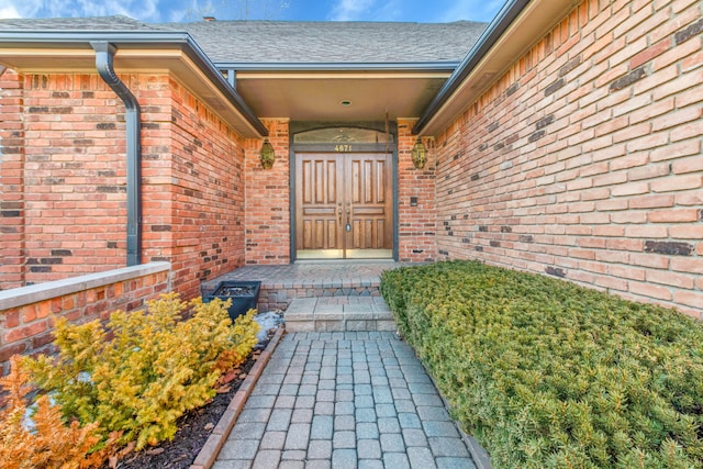 view of exterior entry featuring a shingled roof and brick siding