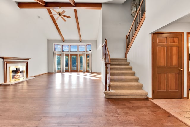 unfurnished living room with high vaulted ceiling, wood finished floors, and a glass covered fireplace