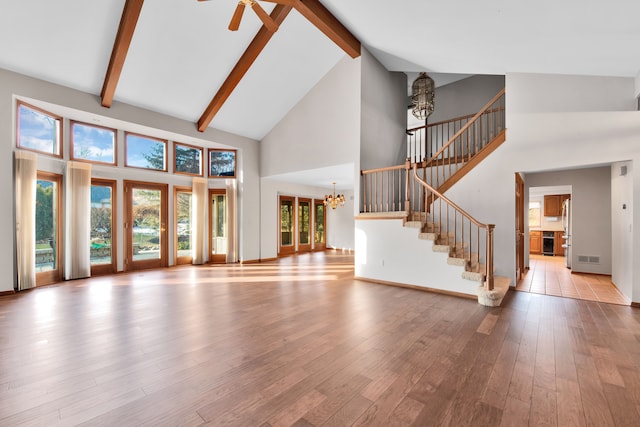 unfurnished living room with stairs, wood finished floors, high vaulted ceiling, beamed ceiling, and ceiling fan with notable chandelier