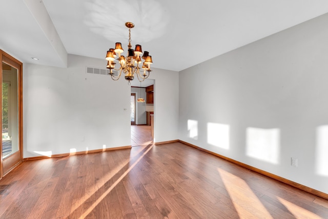 unfurnished room with baseboards, visible vents, hardwood / wood-style floors, and an inviting chandelier