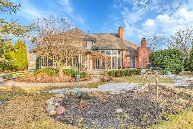 back of house featuring a sunroom, a patio area, a chimney, and brick siding