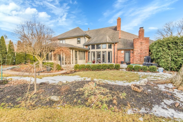 back of property with a sunroom, brick siding, a chimney, and roof with shingles