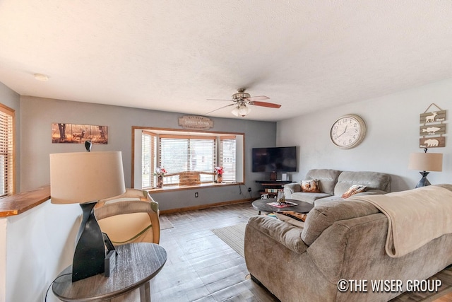 living area with ceiling fan, a textured ceiling, baseboards, and wood finished floors