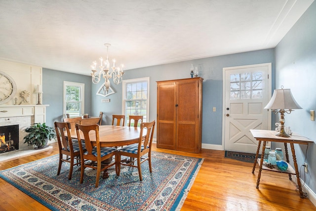 dining room featuring baseboards, light wood finished floors, a tiled fireplace, and a notable chandelier