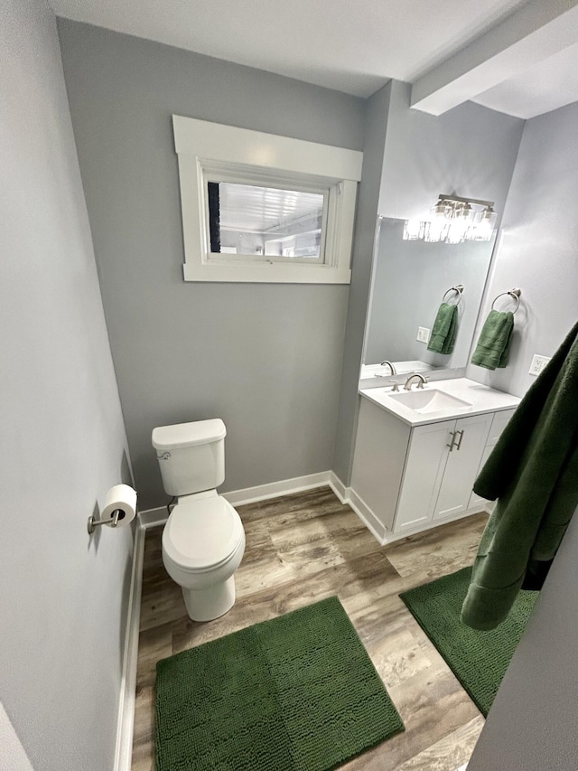 half bathroom with vanity, wood finished floors, toilet, and baseboards