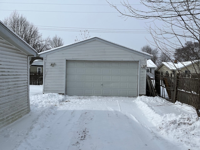 snow covered garage with a detached garage and fence